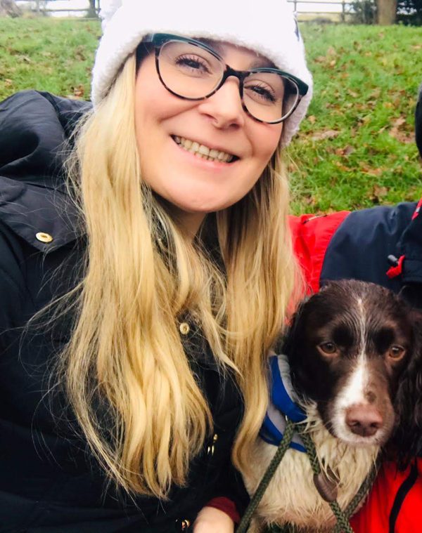 Jo smiling outdoors with her brown and white spaniel